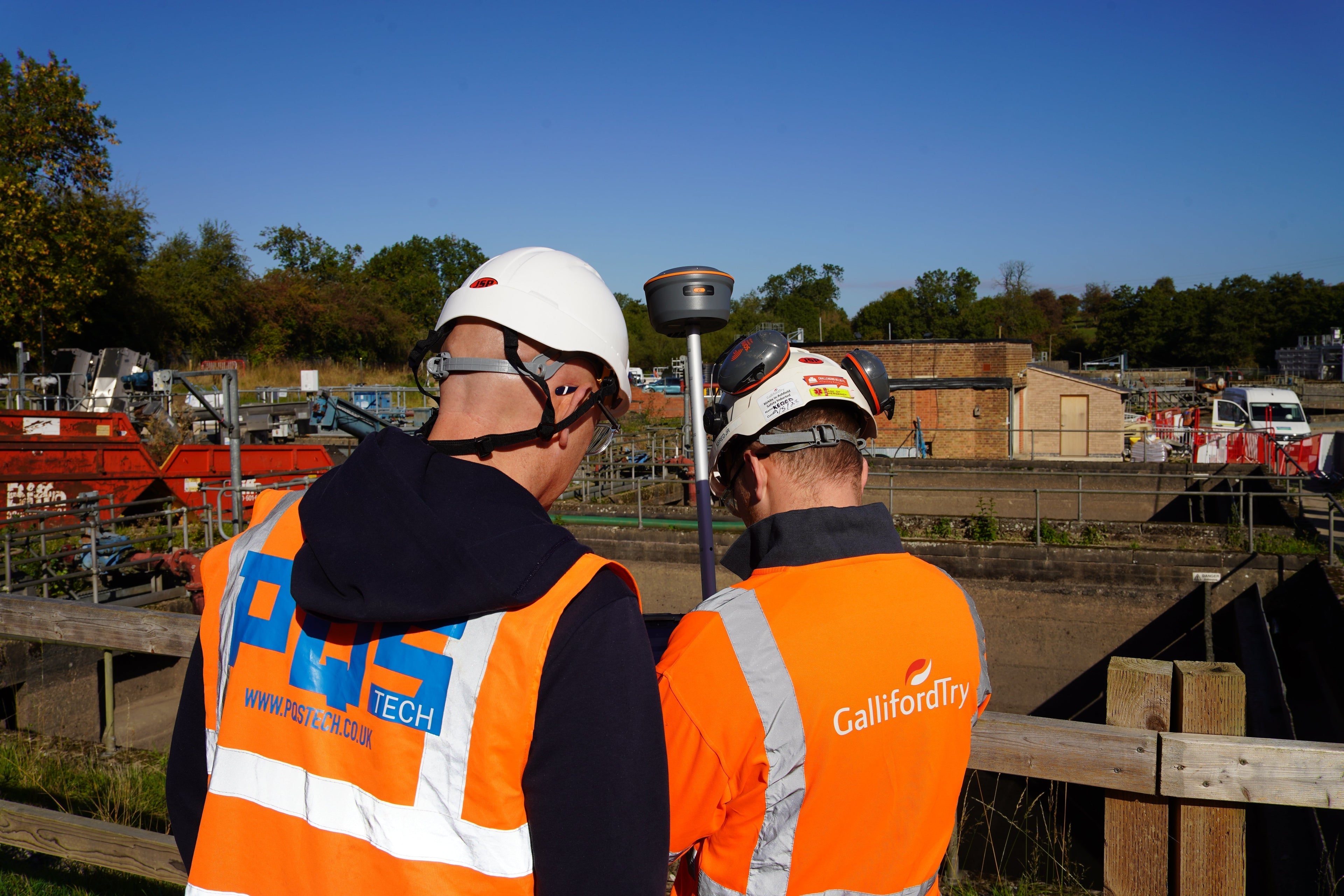 PQS Tech representative and a site engineer collaborating to review land survey data on a CHCNAV GNSS receiver and tablet at an industrial site.