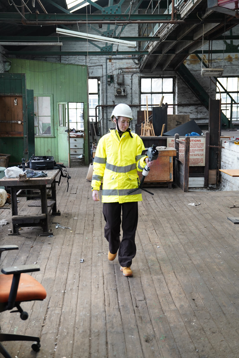Person in a yellow safety vest walking through an industrial area with wooden floors and metal beams and CHCNAV RS7.